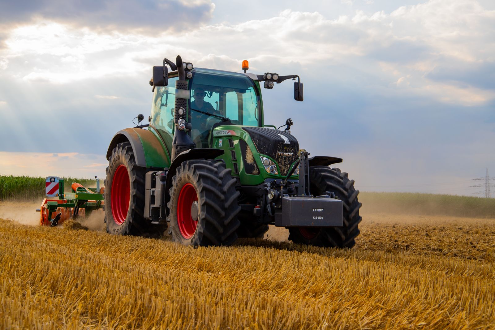 Green tractor plowing a vast field at golden hour